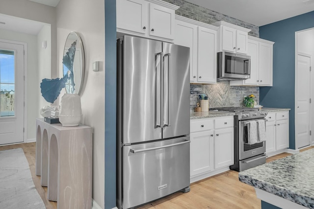 kitchen with light hardwood / wood-style flooring, appliances with stainless steel finishes, white cabinetry, tasteful backsplash, and light stone countertops