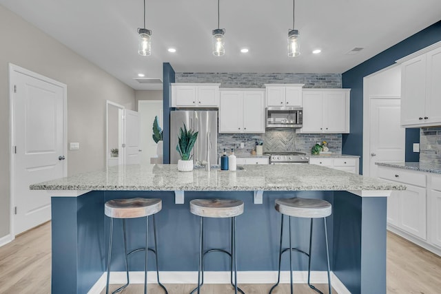 kitchen with white cabinetry, stainless steel appliances, decorative light fixtures, and a center island with sink