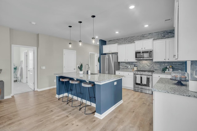 kitchen featuring pendant lighting, a kitchen island with sink, stainless steel appliances, light stone countertops, and white cabinets