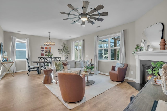 living room featuring a healthy amount of sunlight, ceiling fan with notable chandelier, and light hardwood / wood-style flooring