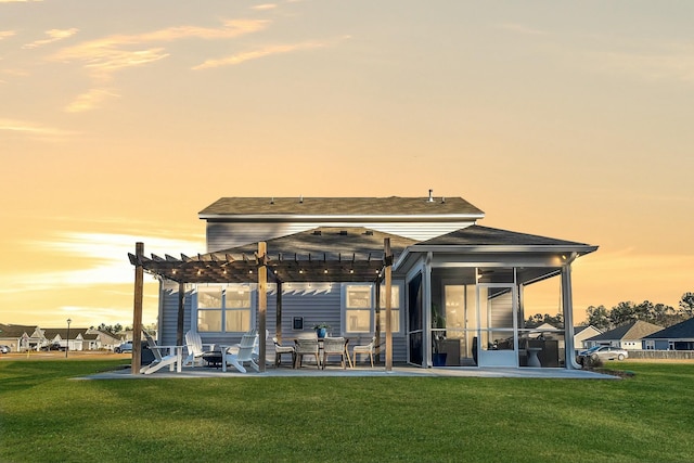 back house at dusk with a pergola, a lawn, a sunroom, and a patio