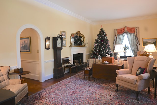 living room featuring a fireplace with raised hearth, crown molding, baseboards, wood finished floors, and arched walkways