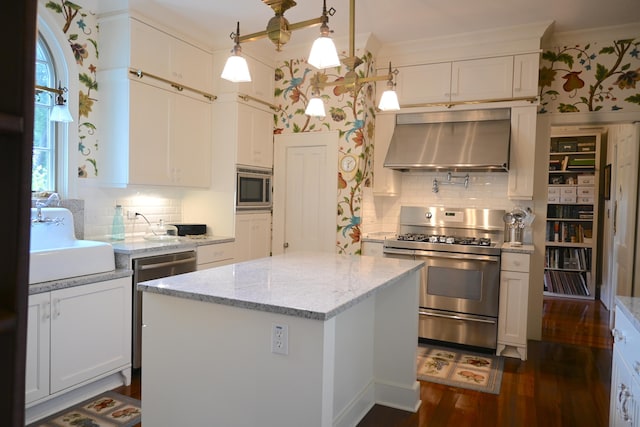 kitchen featuring wallpapered walls, dark wood-style flooring, a sink, stainless steel appliances, and wall chimney exhaust hood