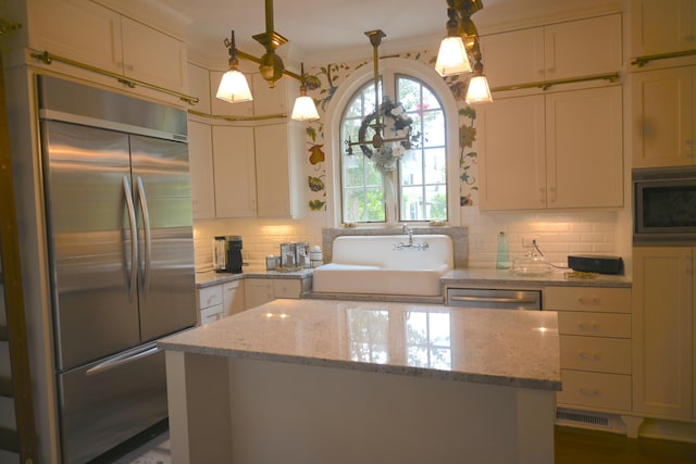 kitchen with tasteful backsplash, a center island, built in appliances, light stone counters, and a sink