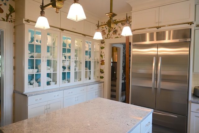 kitchen with stainless steel built in refrigerator, white cabinetry, light stone counters, and decorative light fixtures