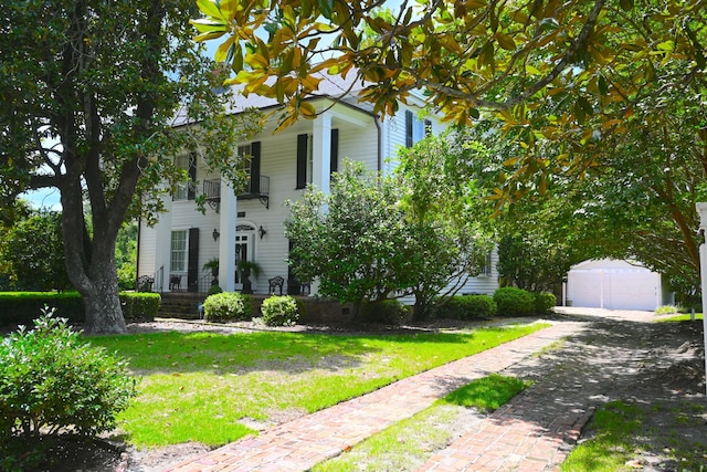 greek revival inspired property with driveway, a balcony, an outdoor structure, and a front lawn