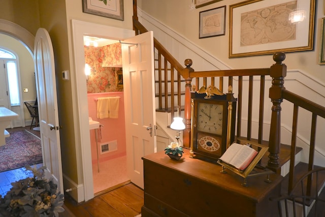 staircase featuring visible vents, a wainscoted wall, wood finished floors, arched walkways, and wallpapered walls