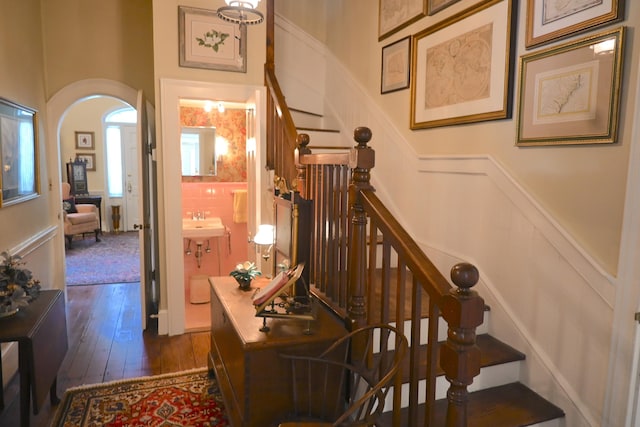 stairs featuring arched walkways, a decorative wall, a wainscoted wall, and hardwood / wood-style flooring