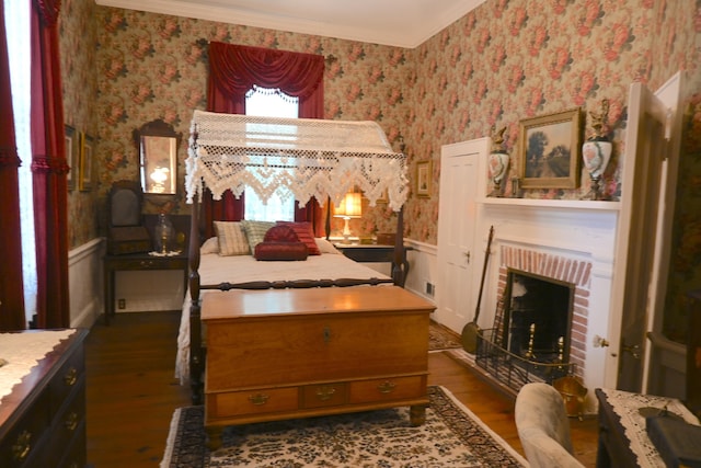 bedroom featuring ornamental molding, wood finished floors, wainscoting, wallpapered walls, and a brick fireplace