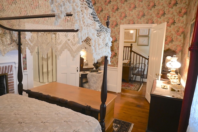 bedroom featuring wallpapered walls, wood finished floors, and wainscoting