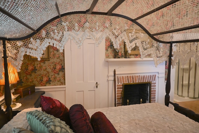 bedroom with a wainscoted wall, a fireplace, and wallpapered walls