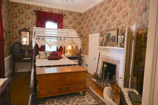 bedroom featuring wood finished floors, a wainscoted wall, wallpapered walls, ornamental molding, and a brick fireplace