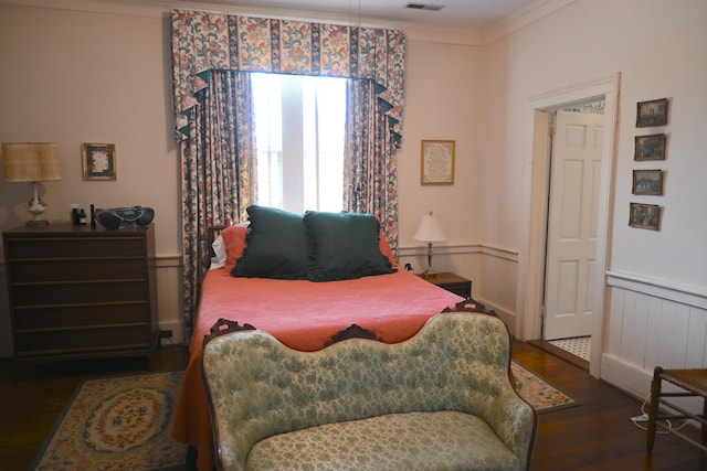 bedroom with a wainscoted wall, crown molding, visible vents, and wood finished floors