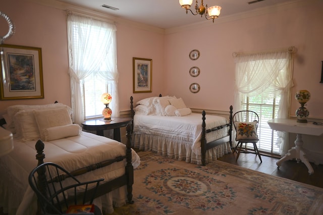 bedroom with visible vents, wood finished floors, ornamental molding, and a chandelier