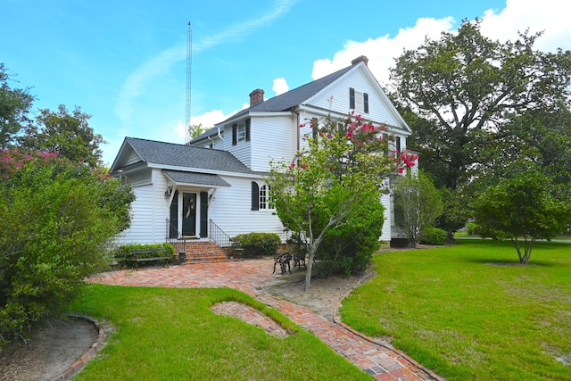 back of house with a patio, a lawn, roof with shingles, and a chimney