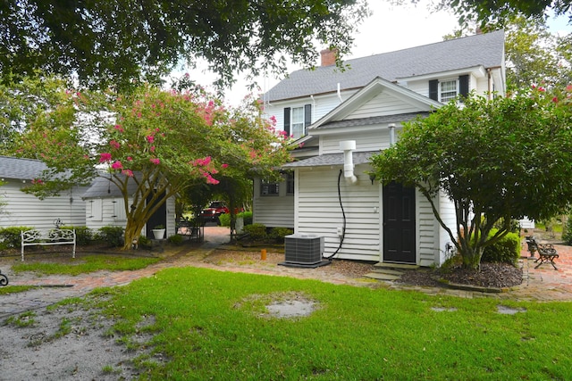 back of property featuring a yard, roof with shingles, central AC unit, and a chimney