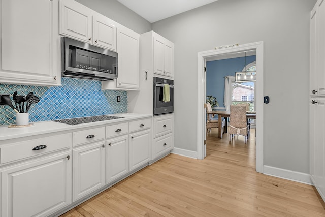 kitchen with oven, white cabinets, stainless steel microwave, black electric stovetop, and light wood-type flooring