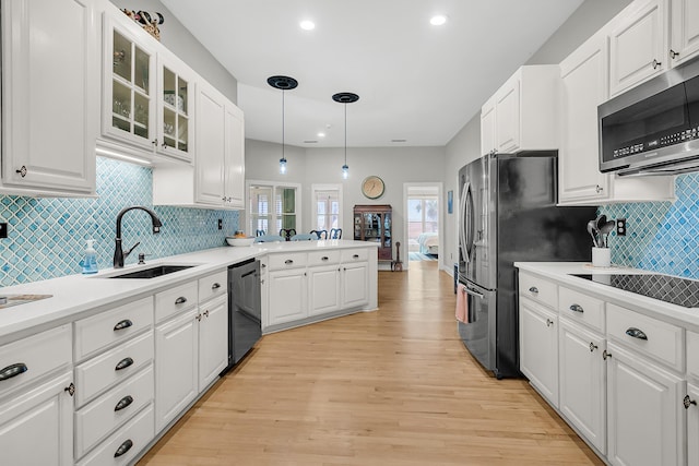 kitchen featuring light wood finished floors, a peninsula, a sink, black appliances, and white cabinets