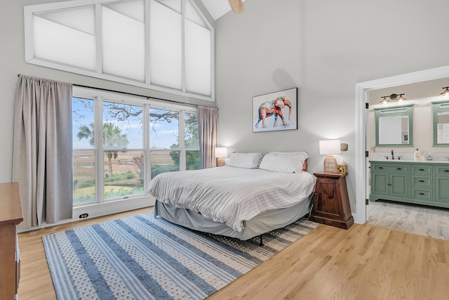 bedroom with high vaulted ceiling, ensuite bathroom, light wood finished floors, and a sink