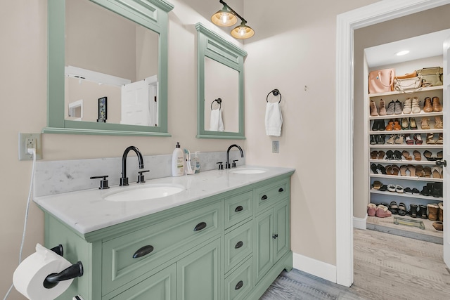 full bath featuring double vanity, wood finished floors, baseboards, and a sink