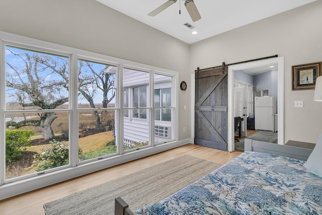 bedroom with visible vents, multiple windows, wood finished floors, freestanding refrigerator, and a barn door