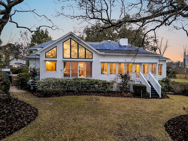 back of house at dusk with a lawn, solar panels, and a chimney