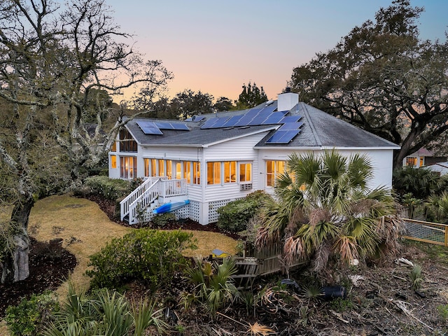 rear view of property featuring stairway, solar panels, a chimney, and roof with shingles