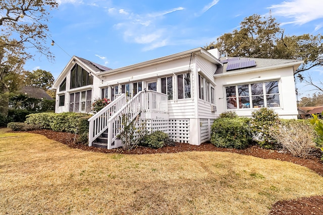 back of house featuring a lawn, roof mounted solar panels, stairway, roof with shingles, and a sunroom