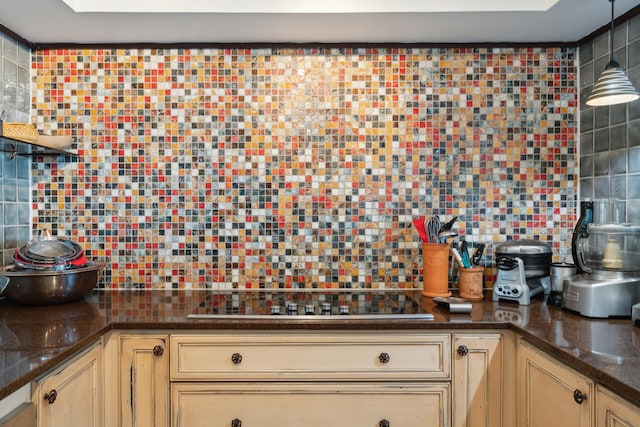 kitchen with black stovetop, decorative light fixtures, backsplash, and dark stone counters