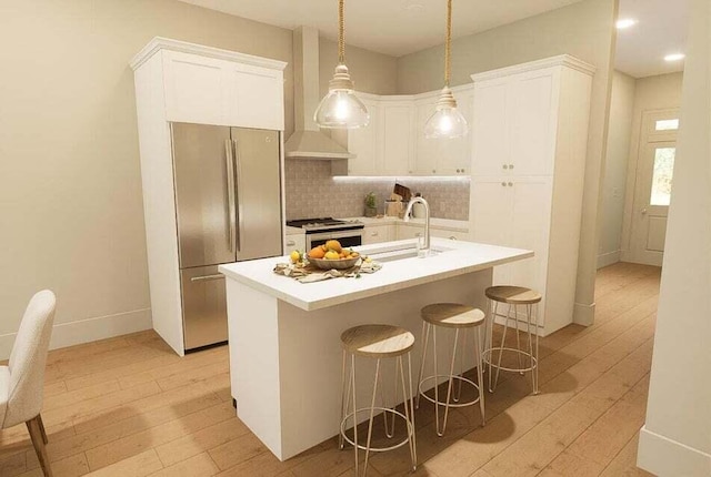 kitchen featuring appliances with stainless steel finishes, light wood-type flooring, a kitchen island with sink, wall chimney range hood, and pendant lighting