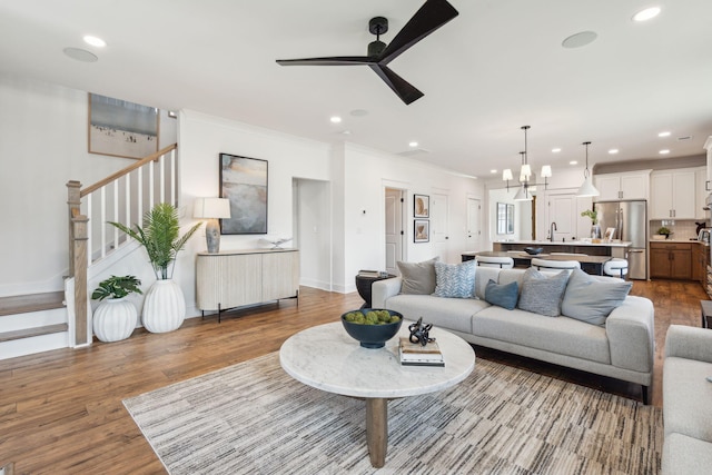 living room featuring wood-type flooring, sink, ceiling fan with notable chandelier, and ornamental molding