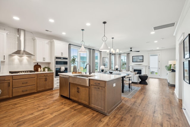 kitchen featuring wall chimney exhaust hood, sink, appliances with stainless steel finishes, an island with sink, and white cabinets