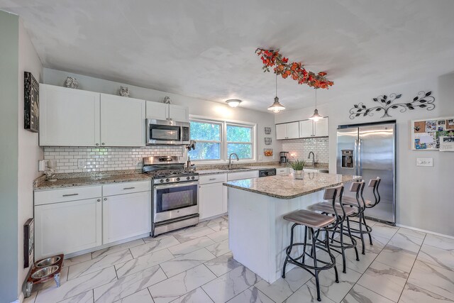 kitchen with appliances with stainless steel finishes, decorative light fixtures, white cabinetry, and a kitchen island