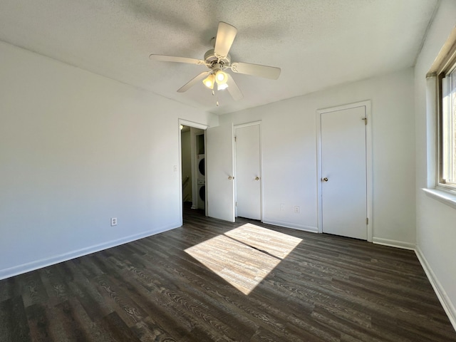 unfurnished bedroom with ceiling fan, dark hardwood / wood-style floors, stacked washing maching and dryer, and a textured ceiling