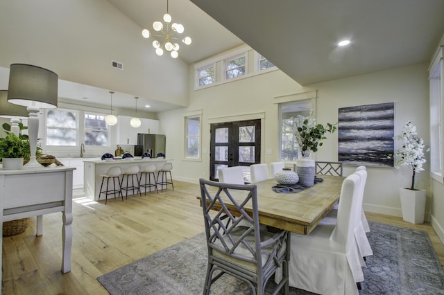 dining room with a wealth of natural light, a notable chandelier, light wood-type flooring, and french doors