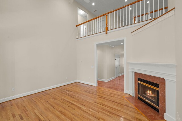 unfurnished living room with a towering ceiling, wood finished floors, a tile fireplace, baseboards, and recessed lighting
