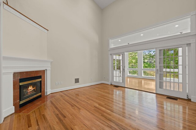 unfurnished living room with wood finished floors, a tiled fireplace, baseboards, and a high ceiling