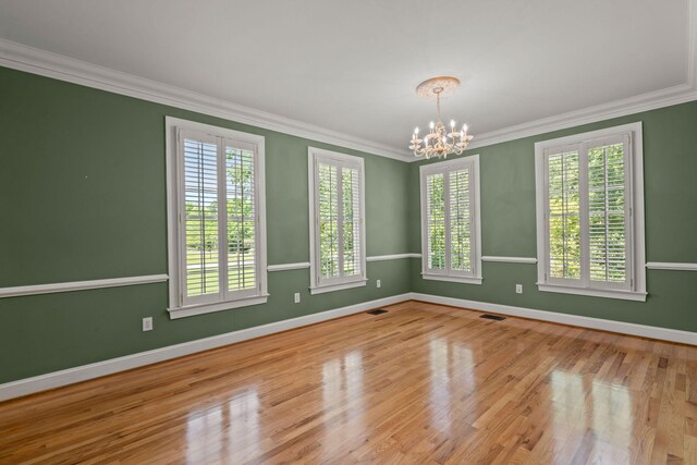 spare room with a chandelier, wood finished floors, ornamental molding, and baseboards