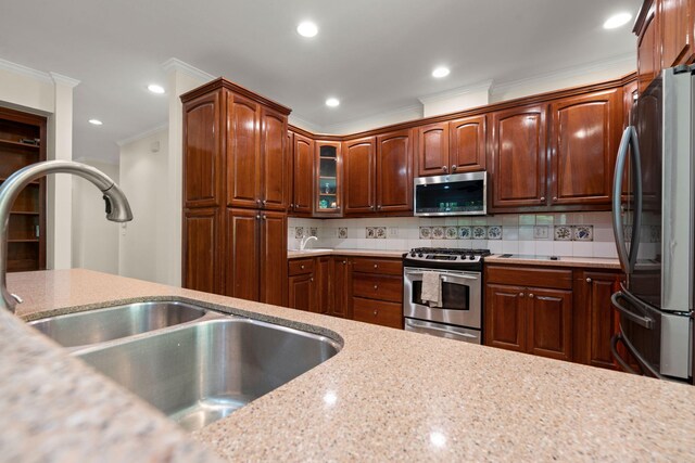 kitchen featuring stainless steel appliances, crown molding, a sink, decorative backsplash, and glass insert cabinets