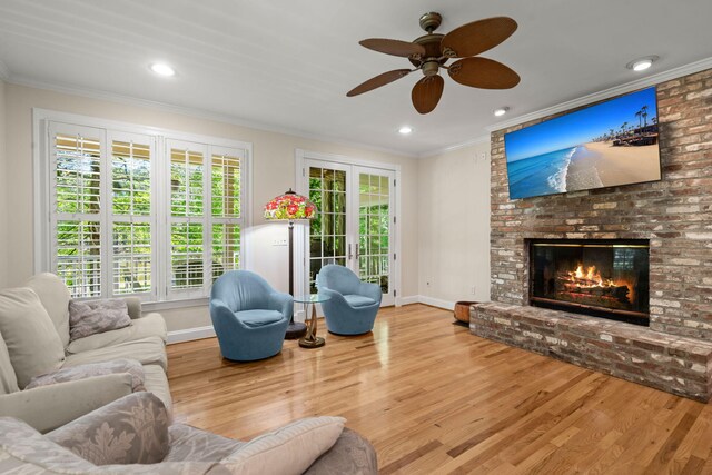 living area with ornamental molding, baseboards, wood finished floors, ceiling fan, and a brick fireplace
