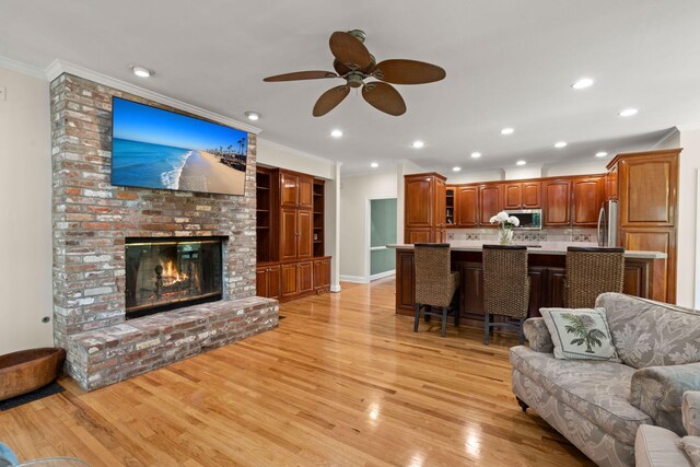 living area featuring ornamental molding, light wood-style flooring, ceiling fan, a brick fireplace, and recessed lighting