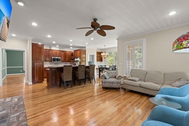 living room featuring crown molding, a ceiling fan, light wood-style flooring, recessed lighting, and a chandelier
