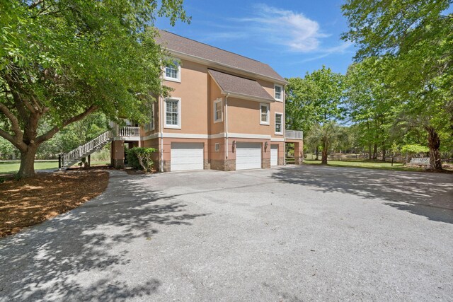 view of side of home with a garage, stone siding, stucco siding, asphalt driveway, and stairway