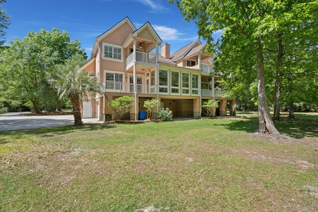 back of property featuring a balcony, ceiling fan, a lawn, driveway, and a sunroom