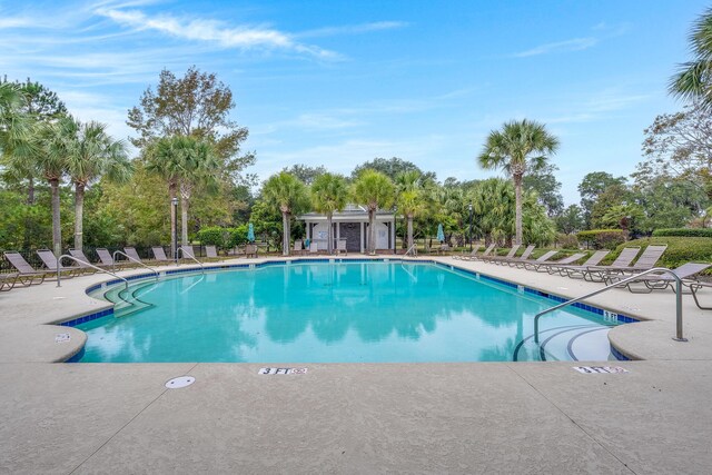 community pool featuring a patio, view of scattered trees, and fence