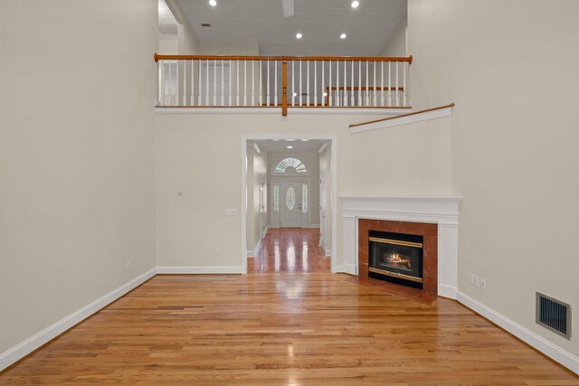 unfurnished living room with wood finished floors, recessed lighting, baseboards, a tile fireplace, and a high ceiling