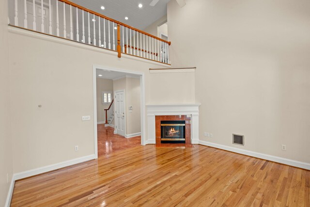 unfurnished living room with a high ceiling, wood finished floors, baseboards, a tile fireplace, and recessed lighting