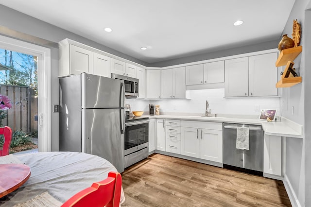 kitchen with light wood-style flooring, a sink, white cabinetry, light countertops, and appliances with stainless steel finishes