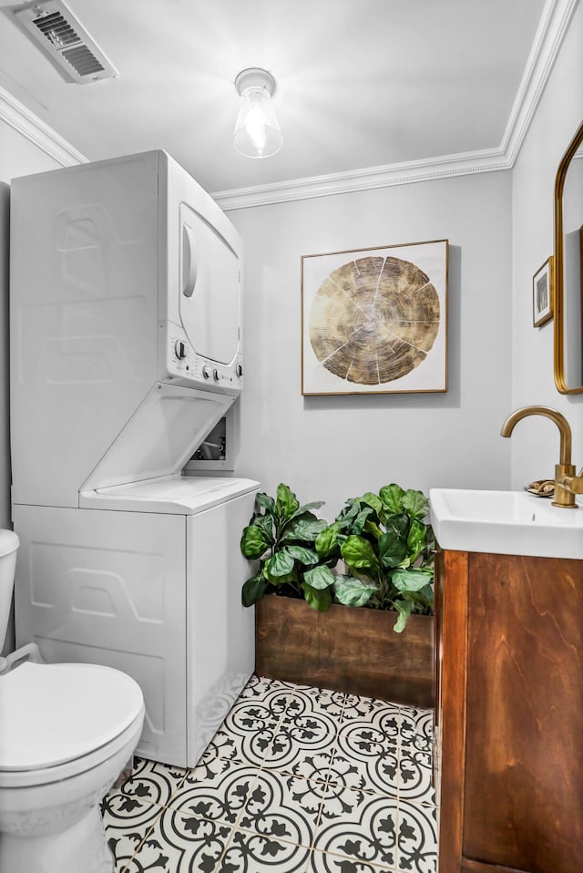 bathroom with visible vents, toilet, stacked washer / drying machine, tile patterned floors, and crown molding