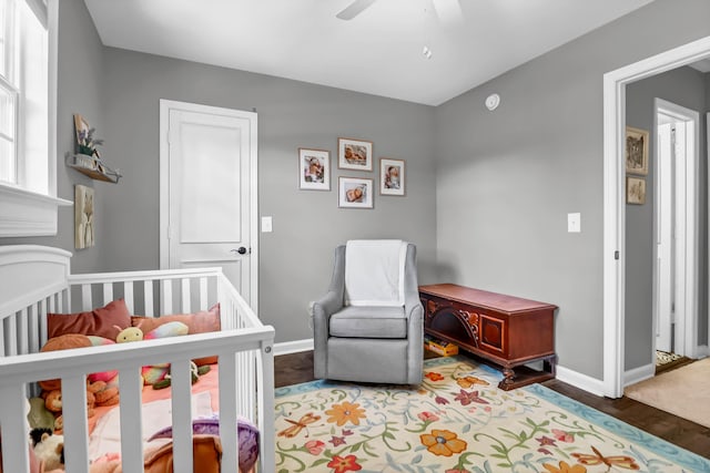 bedroom featuring a ceiling fan, a nursery area, baseboards, and wood finished floors